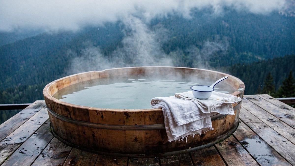 Cedar bathing tub filled with warm mineral water on a wooden terrace above a Carpathian valley